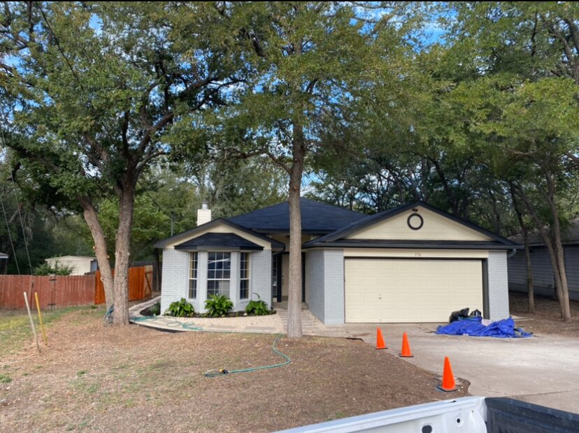 White painted brick home with black roof trim and cream garage doors after repaint