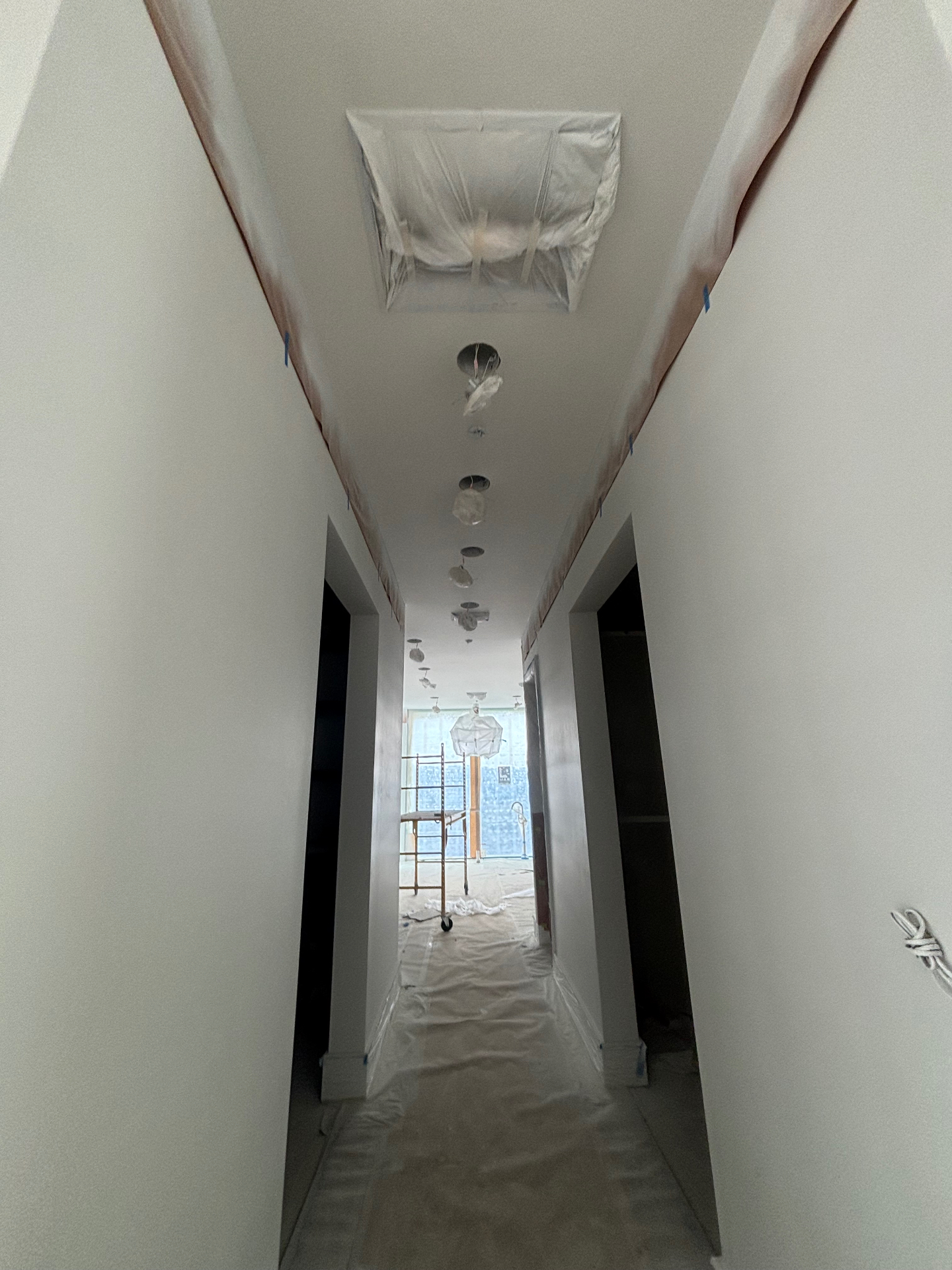 Hallway with freshly sprayed smooth white walls and ceiling, light fixtures still masked