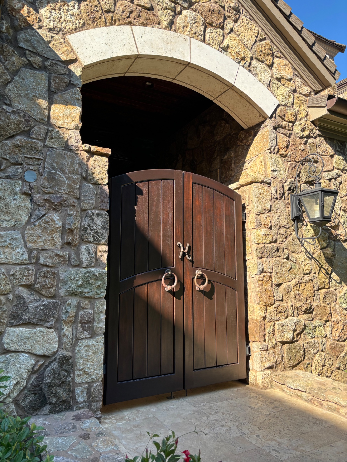 Arched double wood gate with a rich dark stain between stone columns
