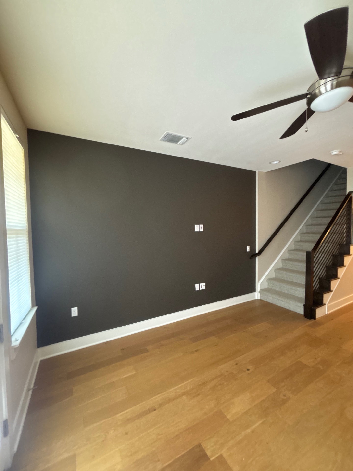 Living room with a smooth charcoal accent wall, white ceiling, wood floors, and staircase