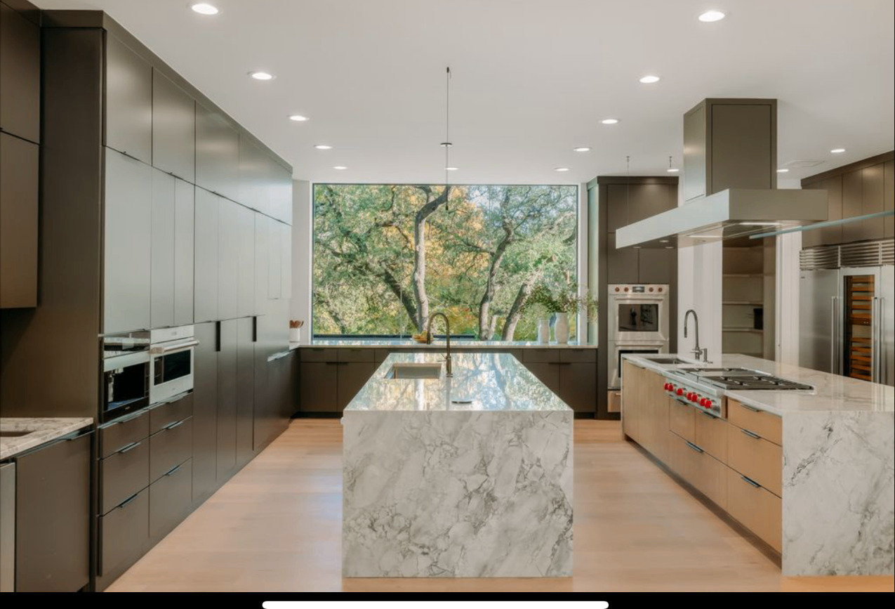 Wide view of a custom home kitchen with dark full-height cabinets and a marble waterfall island