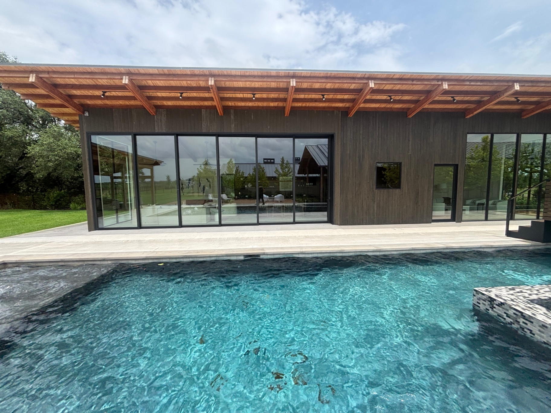 Poolside pavilion with stained vertical wood siding and timber rafters