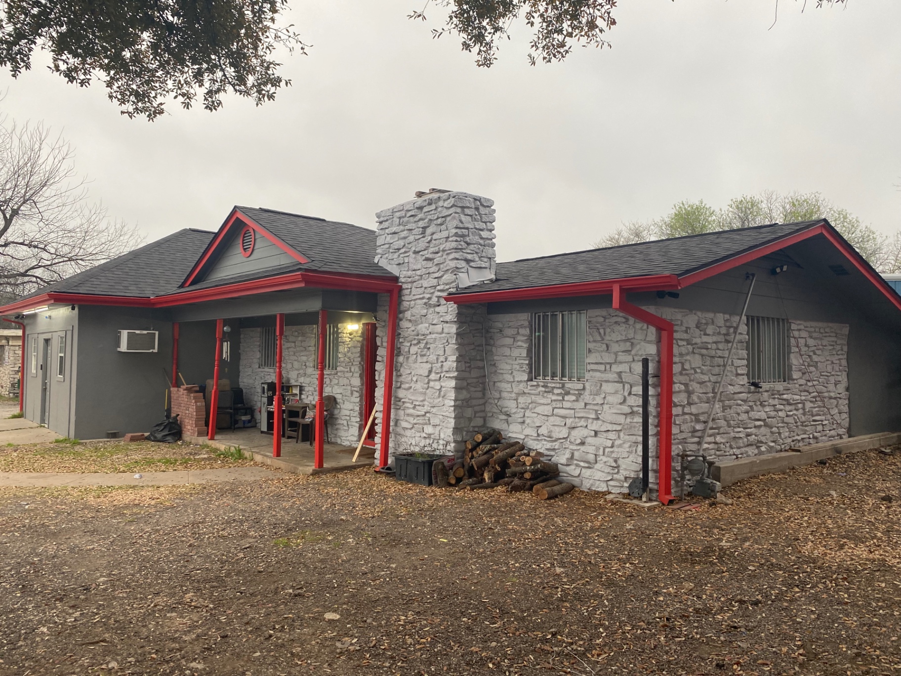 Stone ranch home with red gutters, fascia, and porch posts painted by JJY Painting